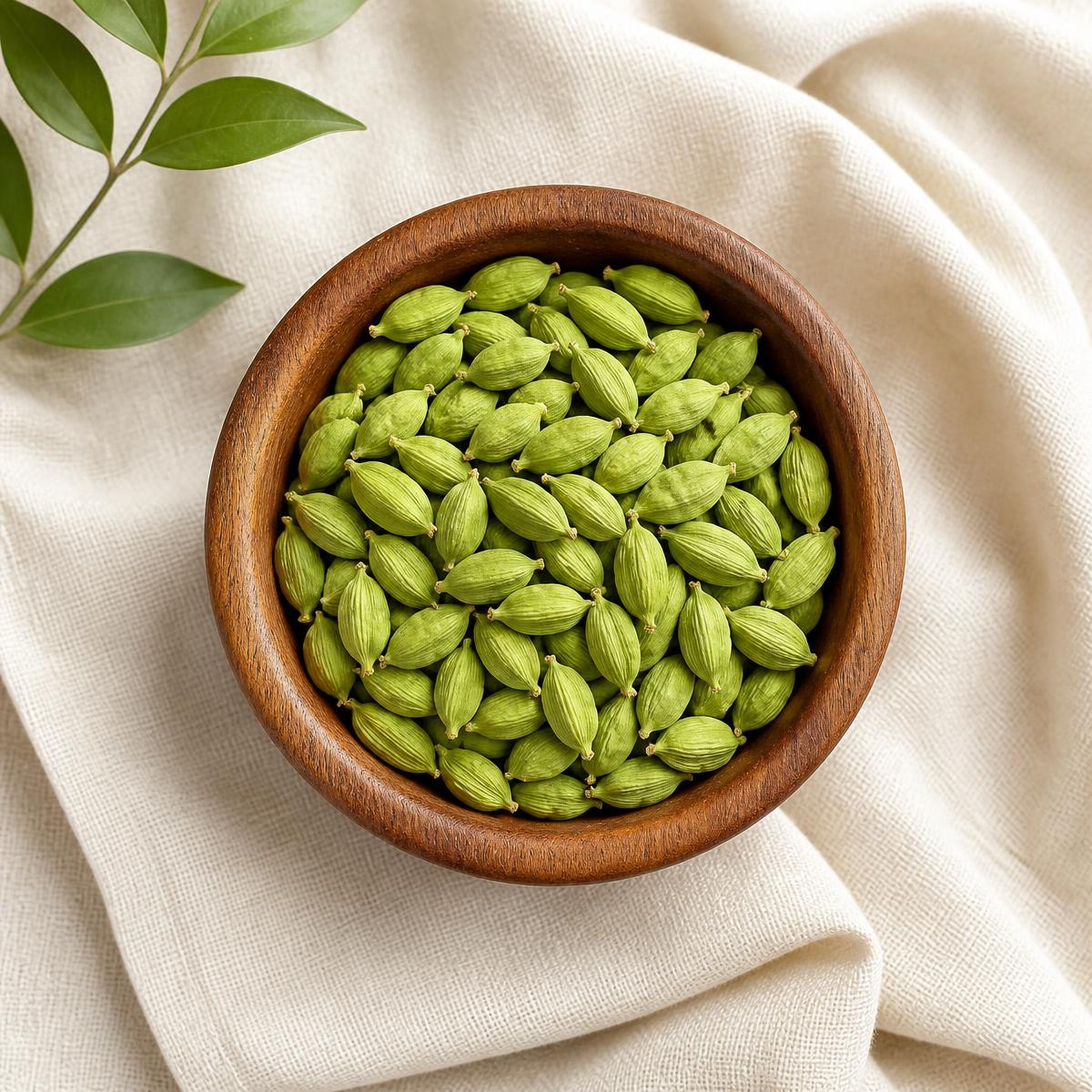 Green cardamom pods in a wooden bowl on cream linen